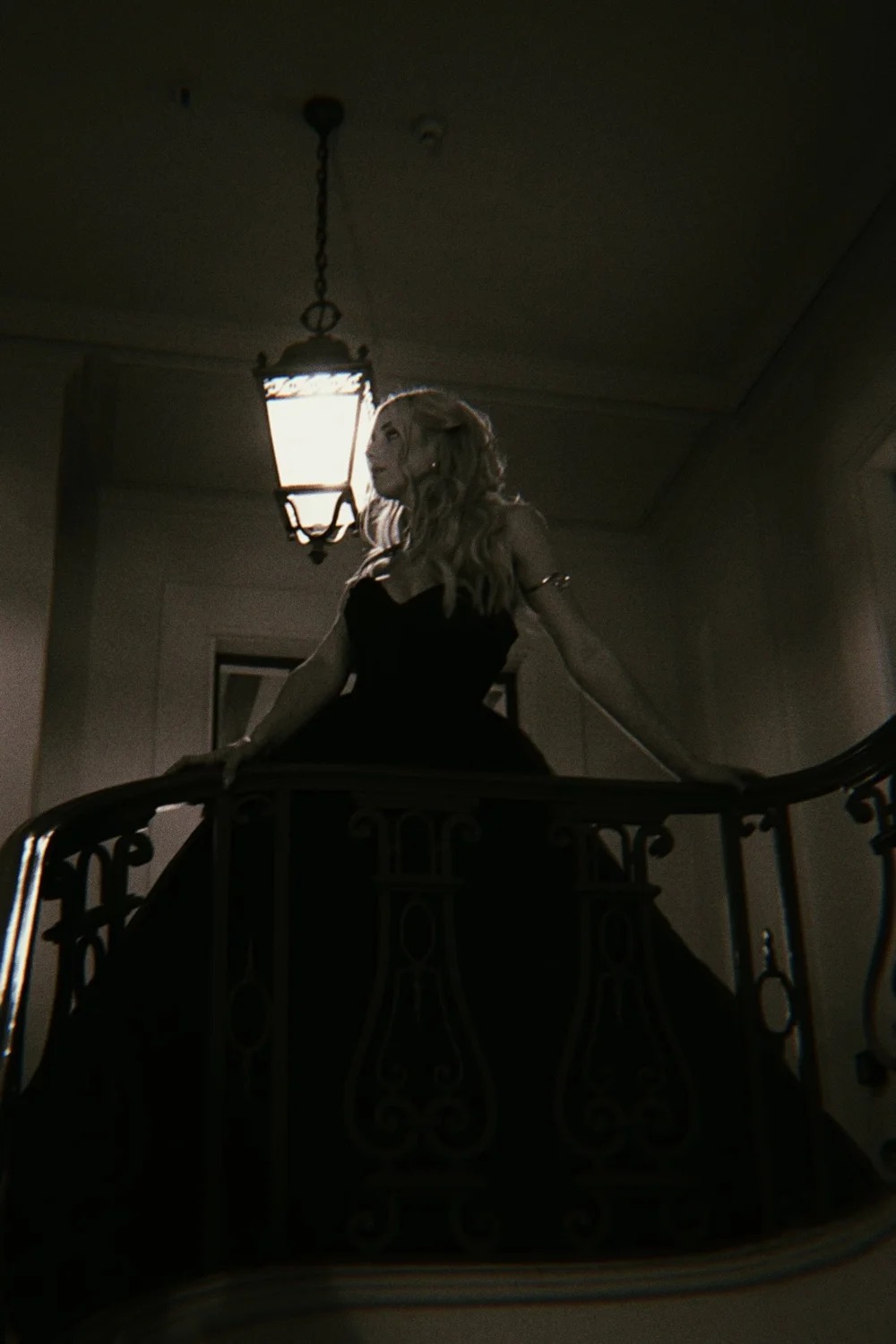 Zoe in a black dress on a balcony beneath a hanging lantern